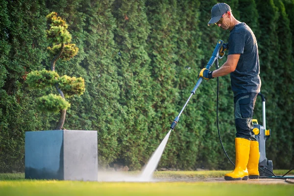Professional Landscaper Using a Pressure Washer to Clean Garden Paths in a Residential Yard
